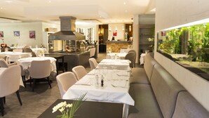 A restaurant with tables set for dining, a kitchen area, and a large aquarium. - Logis Hotel la Résidence (Le Val-d'Ajol)
