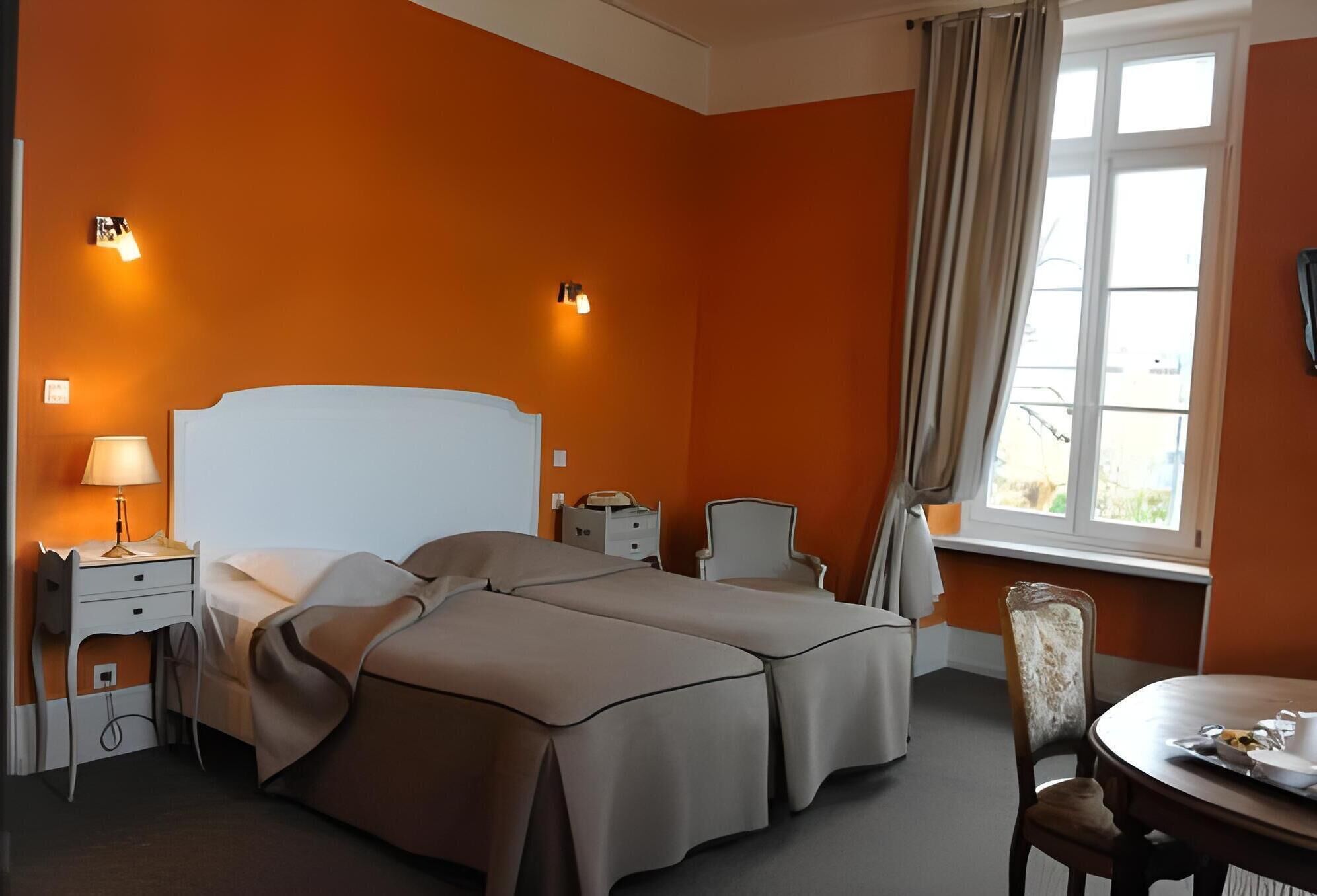 A hotel room with two beds, a desk with a lamp, a chair, a dining table with a tray, and a window with curtains.
