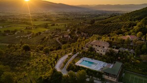 An aerial view of a villa with a swimming pool, surrounded by lush greenery and hills.