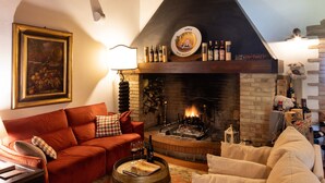 A cozy living room with a fireplace, wooden beams, a red sofa, and a beige armchair.