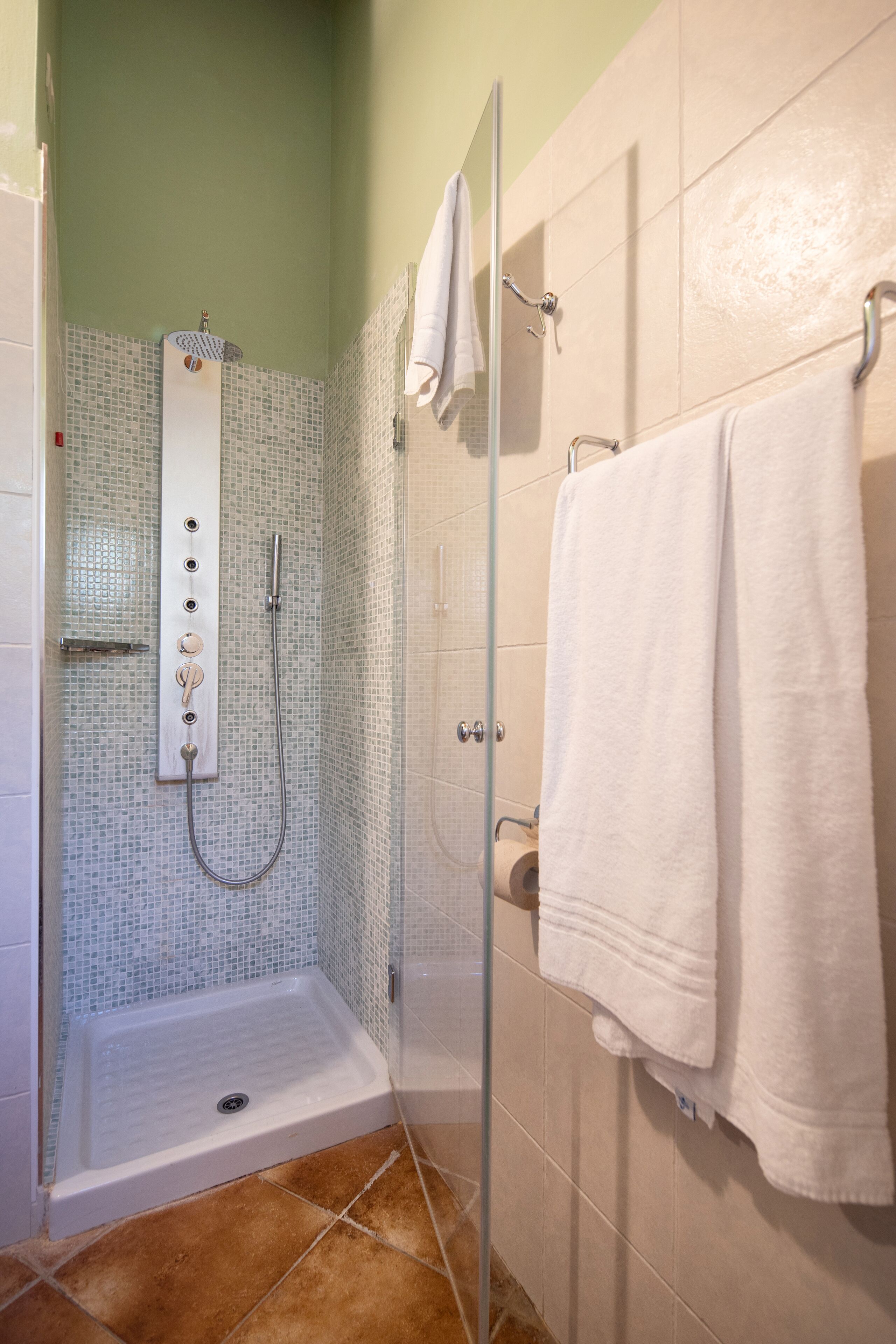 A walk-in shower with a glass door, a tiled wall, and a white towel hanging on the wall.