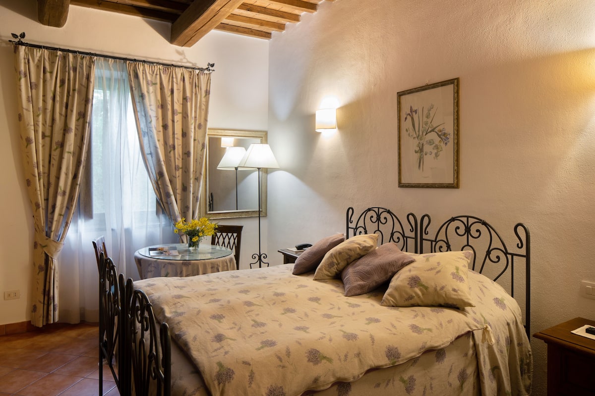 Une chambre à coucher avec un lit, une table de chevet, une lampe, une chaise et une fenêtre avec des rideaux.