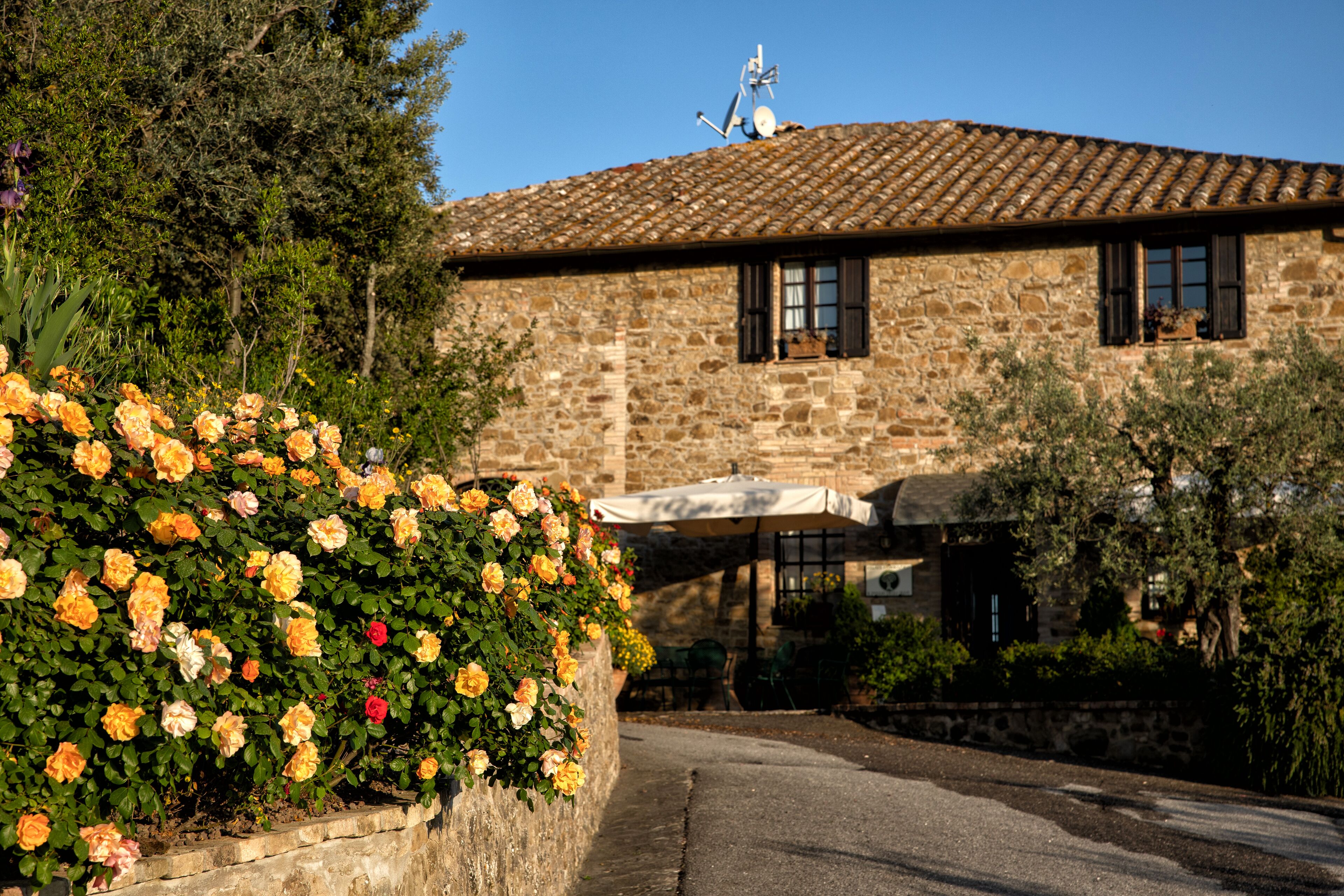 A stone building with a tiled roof, a garden with roses, and outdoor seating.