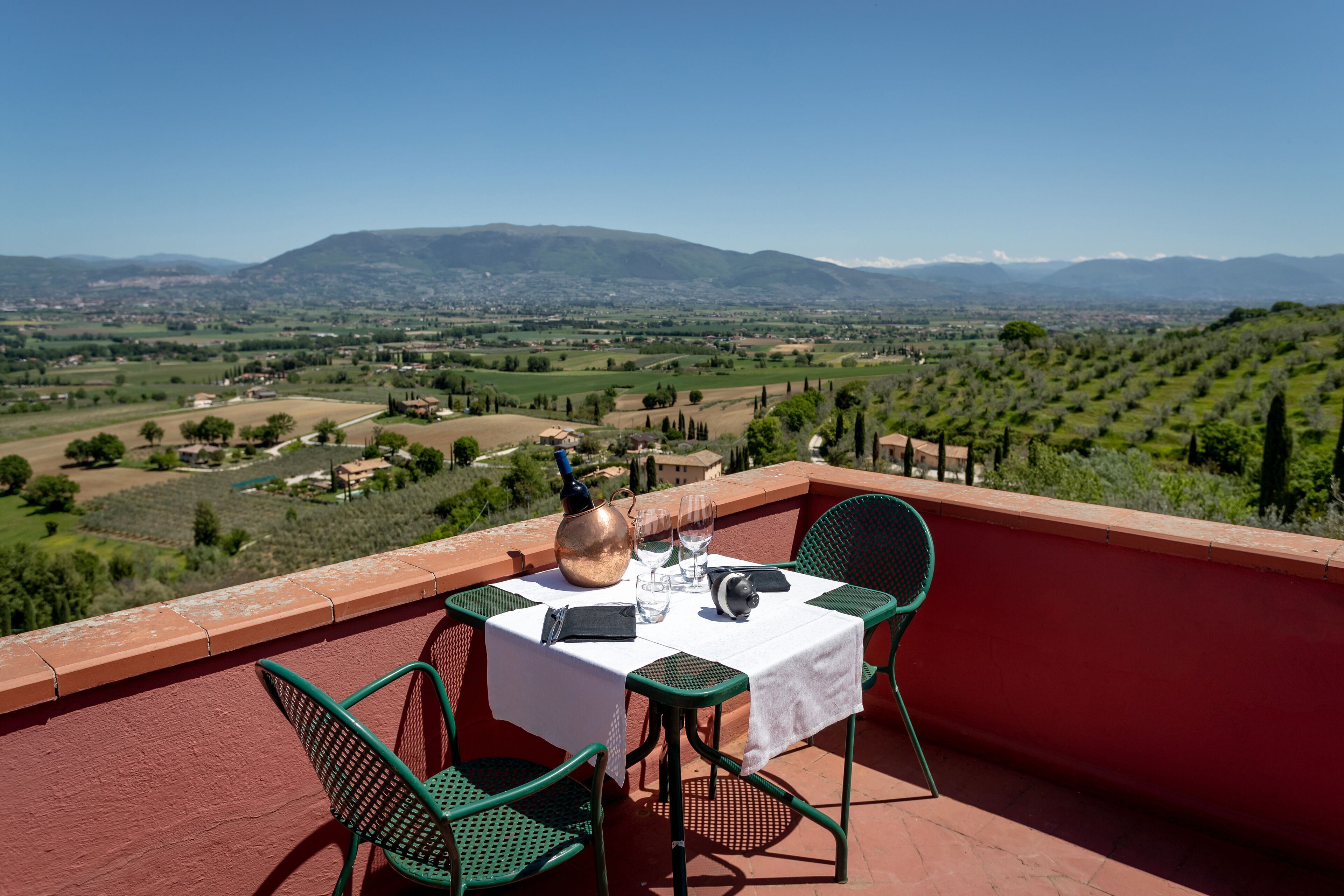 Une table dressée sur un balcon, offrant une vue sur un vignoble et des montagnes lointaines.