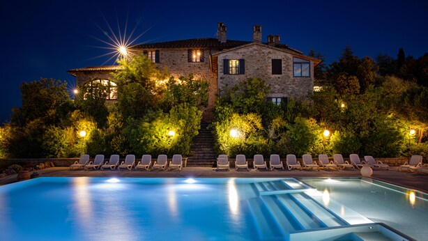A stone building with a swimming pool and lounge chairs.