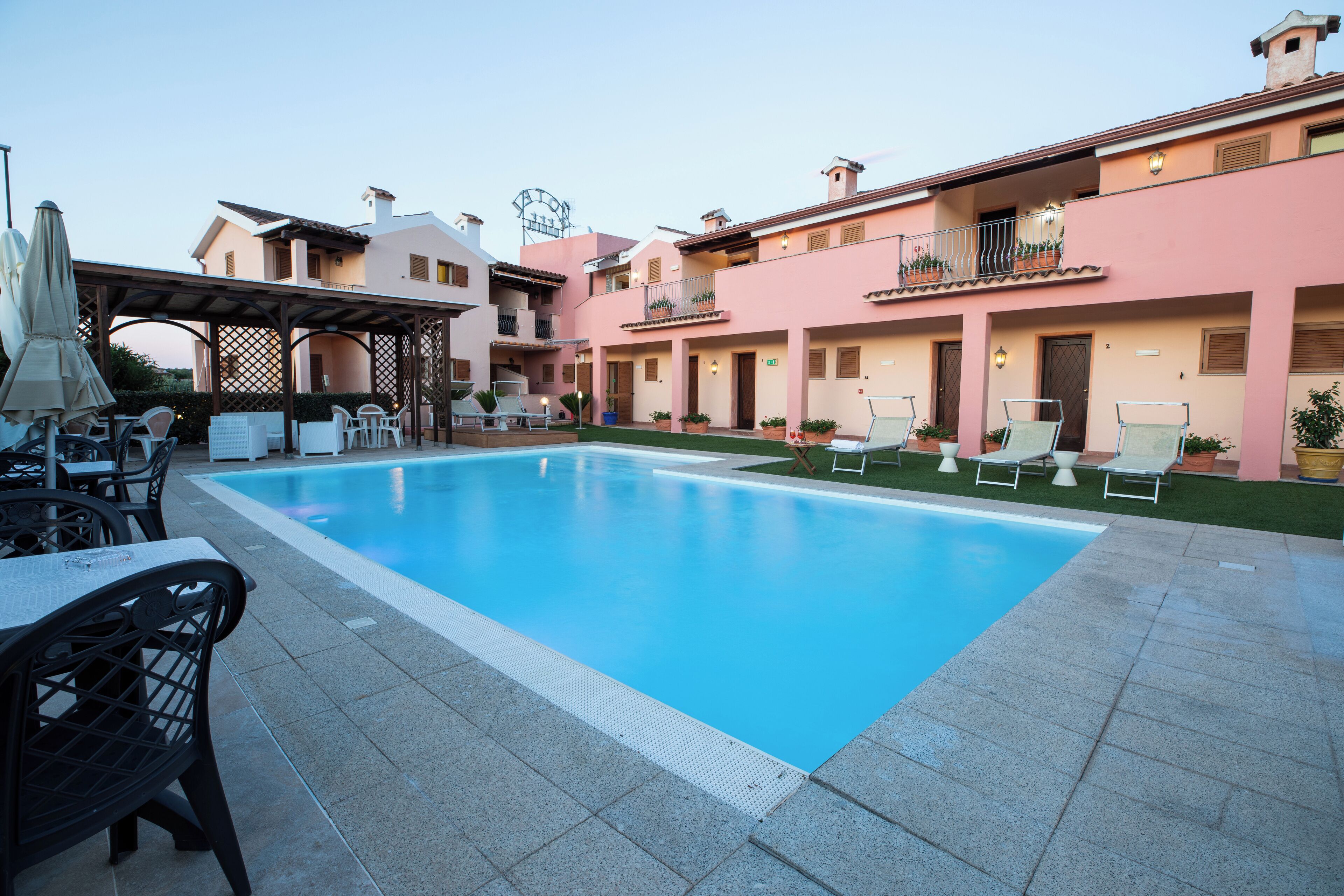 Une piscine entourée de chaises longues et de parasols, elle-même bordée d’immeubles dotés de balcons et de plantes en pot.