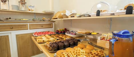 A buffet with various food items including waffles, pastries, and fruits.