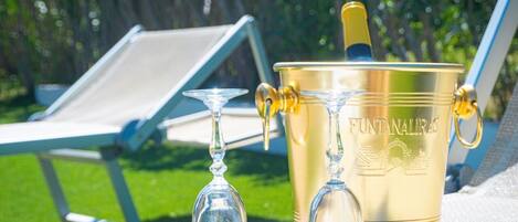 A sunlit outdoor setting with a gold bucket labeled 'FUNTANALIRAS' and two clear wine glasses on a table.