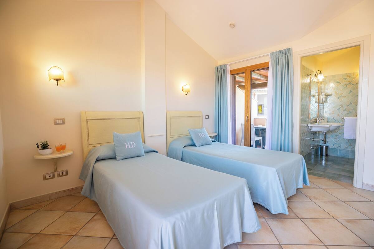 A hotel room with two beds, a small bedside table with a plant, and a bathroom visible through an open door.