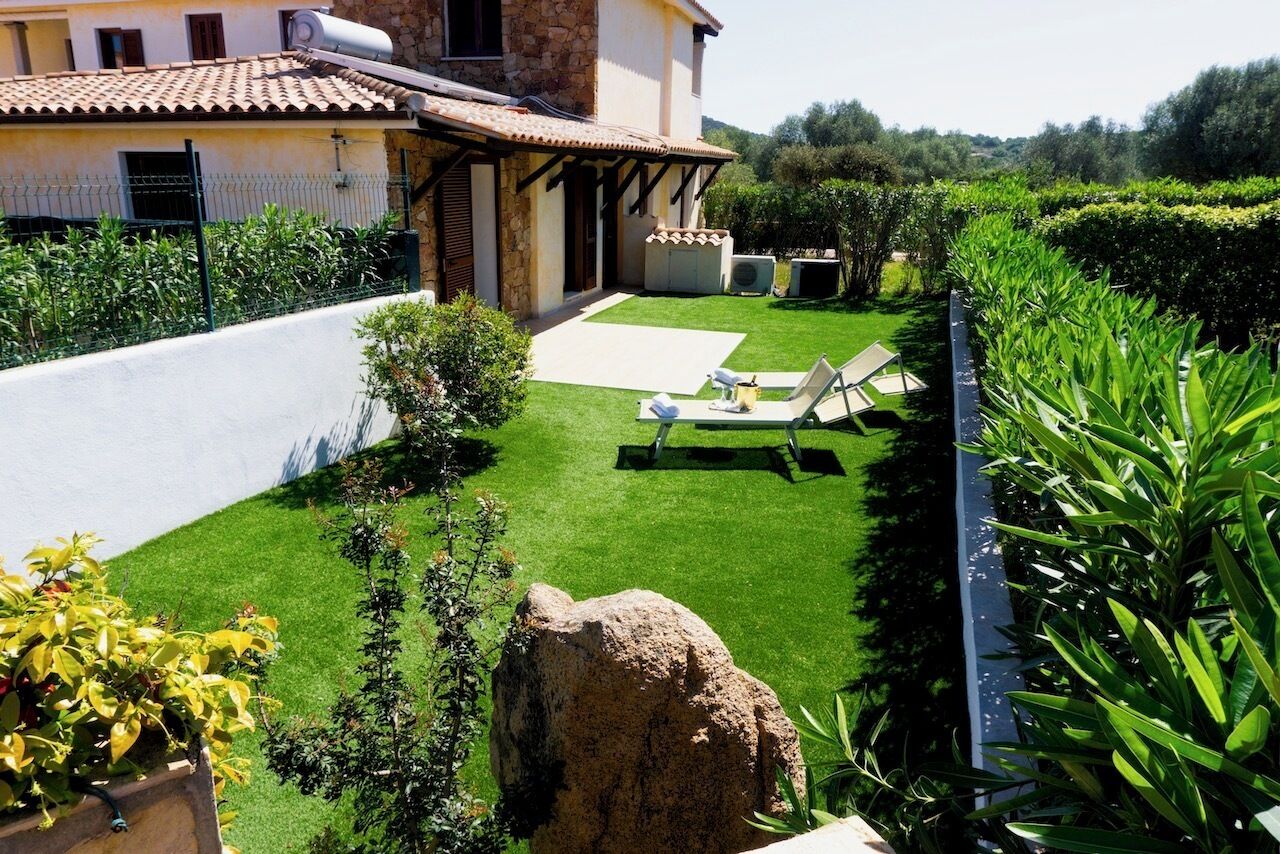 Ein gepflegter Garten mit einer Terrassenfläche, einem großen Felsen und einem Gebäude mit einem Ziegeldach.