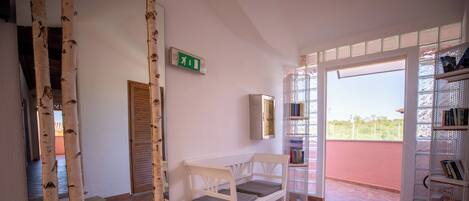 A room with a white bench, a bookshelf, and a door with a green exit sign.