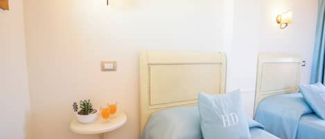 A hotel room with two beds, a small bedside table with a plant and a glass of orange juice, and wall-mounted light fixtures.