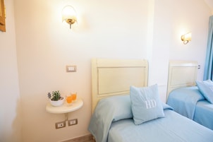 A hotel room with two beds, a small bedside table with a plant and a glass of orange juice, and wall-mounted light fixtures.