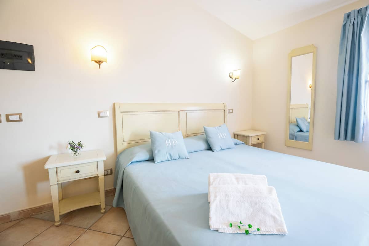 A neatly arranged bedroom with a bed, bedside tables, a mirror, and a wall-mounted light fixture.