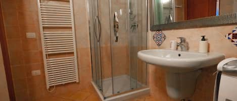 A bathroom with a glass shower enclosure, a sink with a mirror, and a towel rack.
