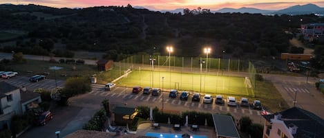 A tennis court surrounded by parked cars and residential buildings.