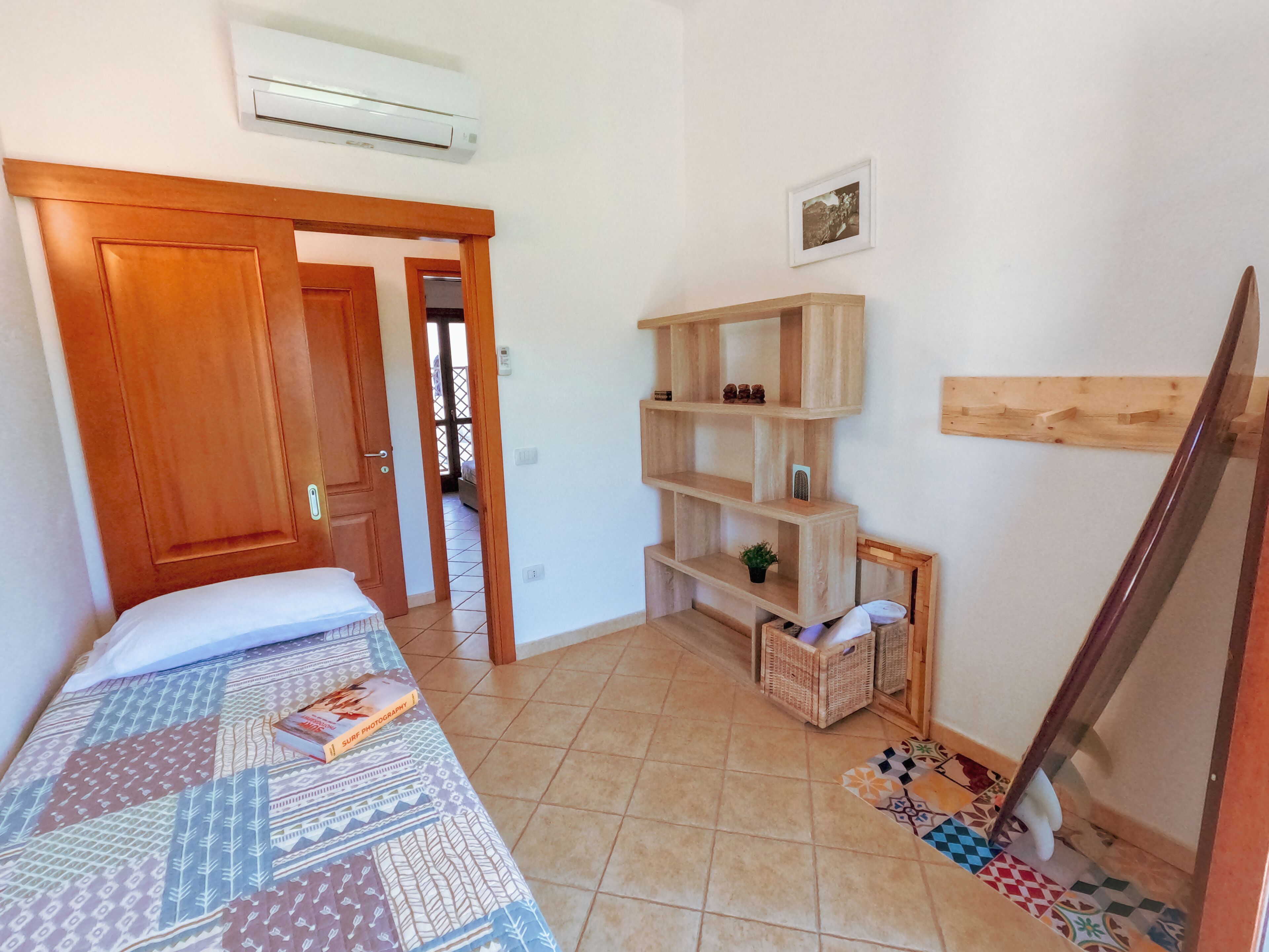 Une chambre à coucher avec un lit, une porte en bois, une étagère et un sol carrelé.