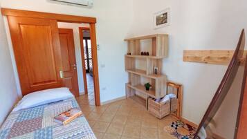 Une chambre à coucher avec un lit, une porte en bois, une étagère et un sol carrelé.