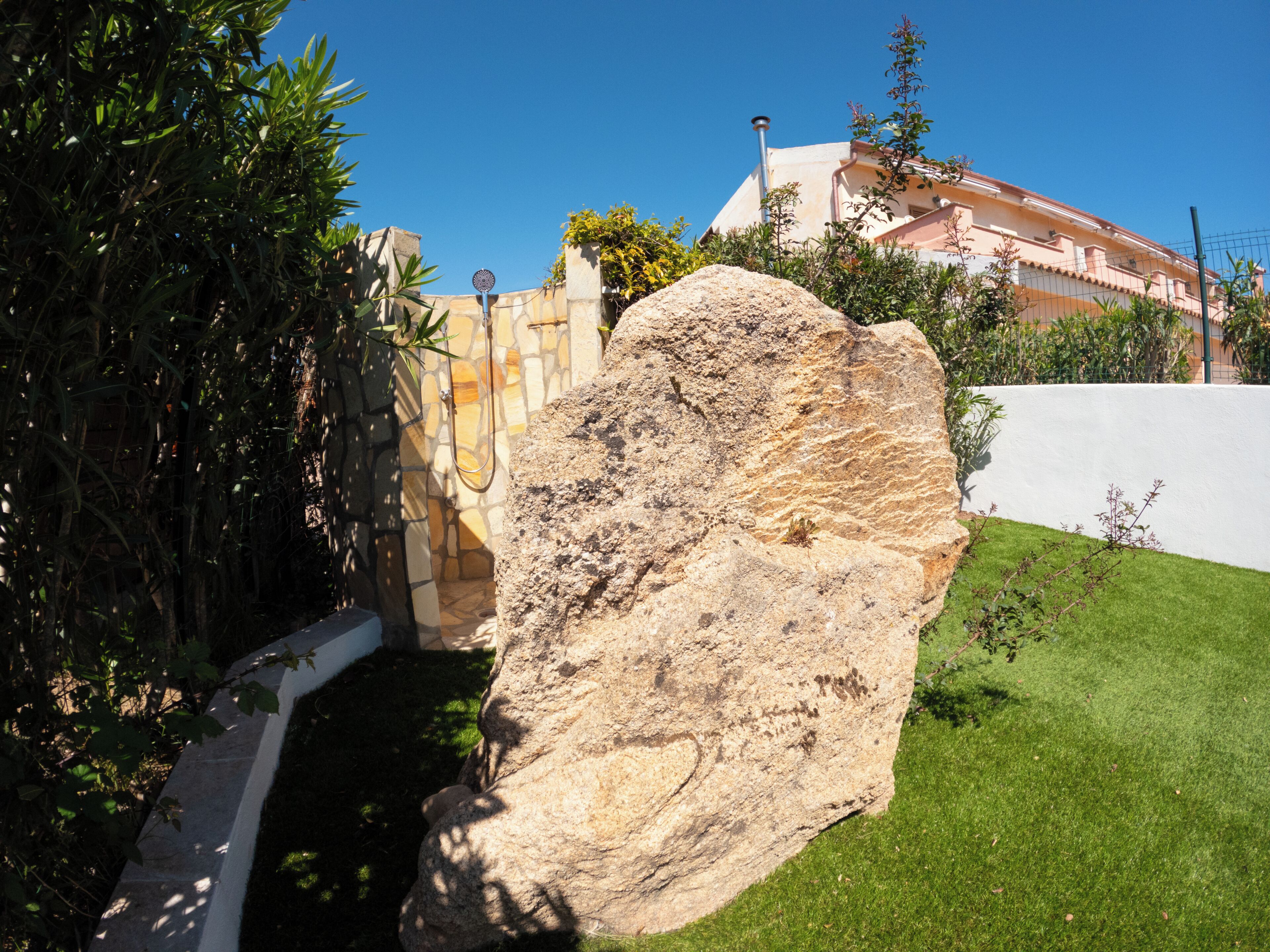Una gran roca en un jardín ajardinado con un muro de piedra y un edificio al fondo.