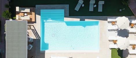 Vue aérienne d’un espace piscine sur le toit, avec des chaises longues et des parasols.
