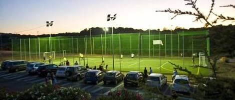 Ein Sportplatz mit grünem Zaun, Toren und einem Parkplatz mit Autos.