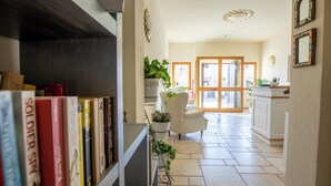 A well-lit hallway with a bookshelf, a white chair, and a potted plant. - Hotel Daniel (Olbia)