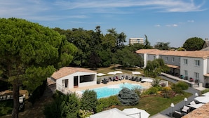 A pool area with lounge chairs and umbrellas, surrounded by trees and buildings. - LOGIS HOTEL LE RABELAIS (Fontenay-le-Comte)