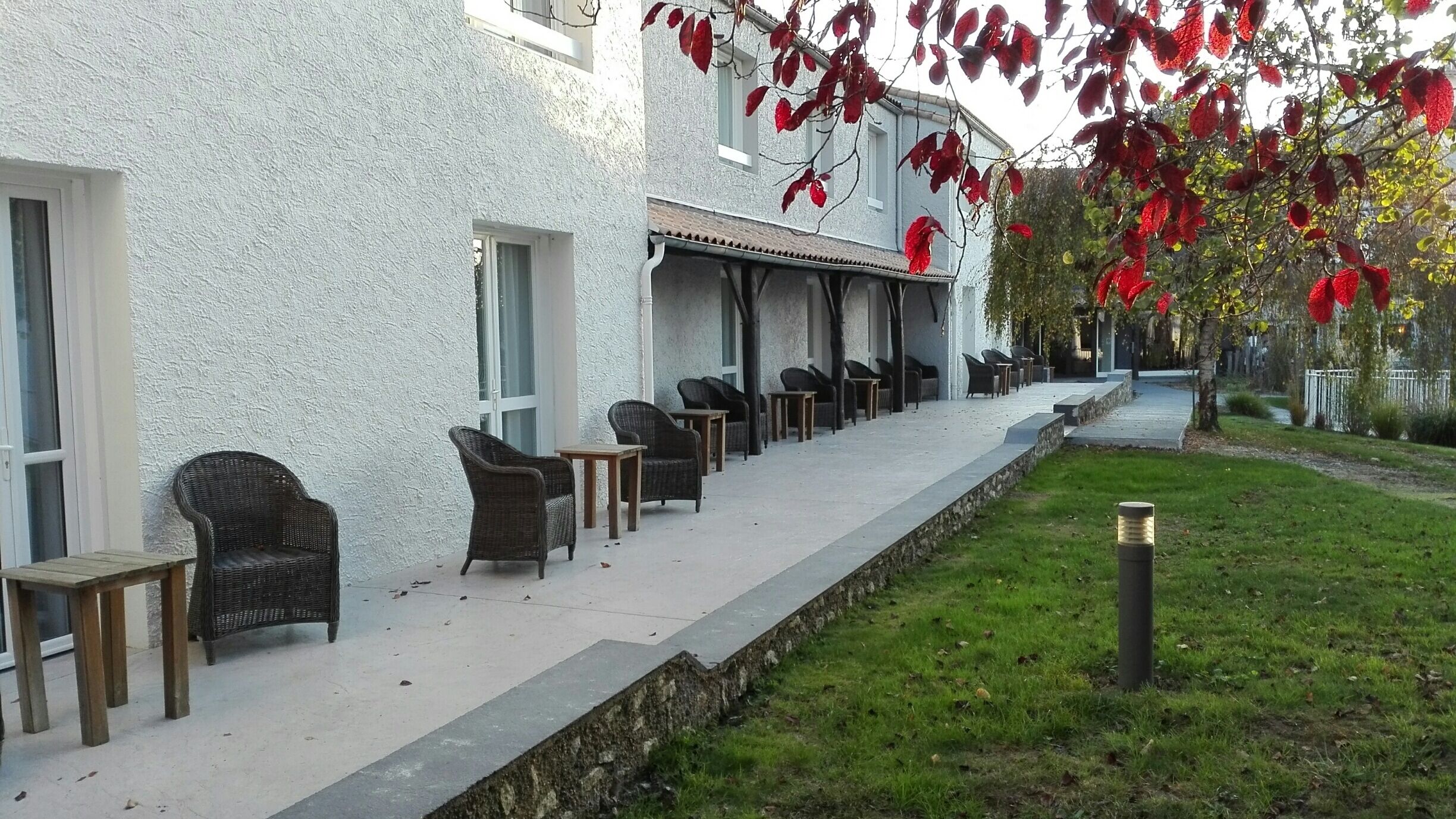 Een gebouw met een overdekt terras met rieten stoelen en tafels.