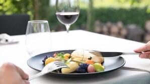 A dining table with a plate of food, a fork, and a glass of red wine.