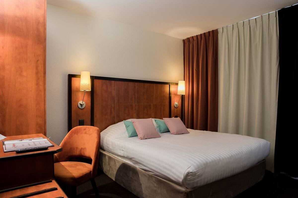 Habitación de hotel con cabecera de madera, un escritorio con silla y una cama con almohadas.