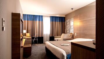 A hotel room with a bed, a desk, a chair, a sofa, and a patterned wall.