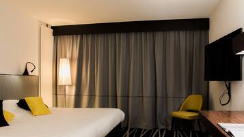 A hotel room with a bed, a desk, a chair, a TV, and a window with curtains.