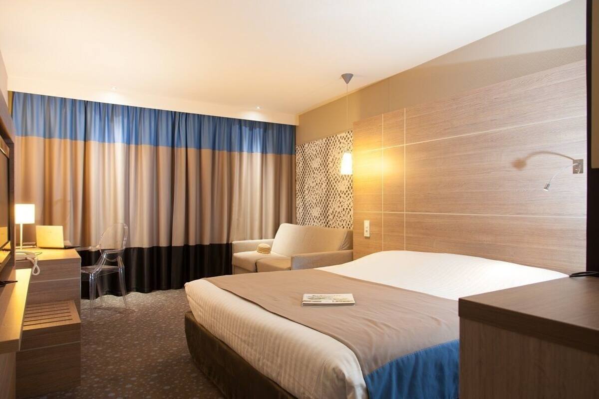 Una habitación de hotel con una cama, un escritorio, una silla y una lámpara.