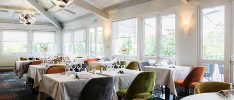A restaurant with multiple tables and chairs, large windows, and hanging spherical light fixtures.