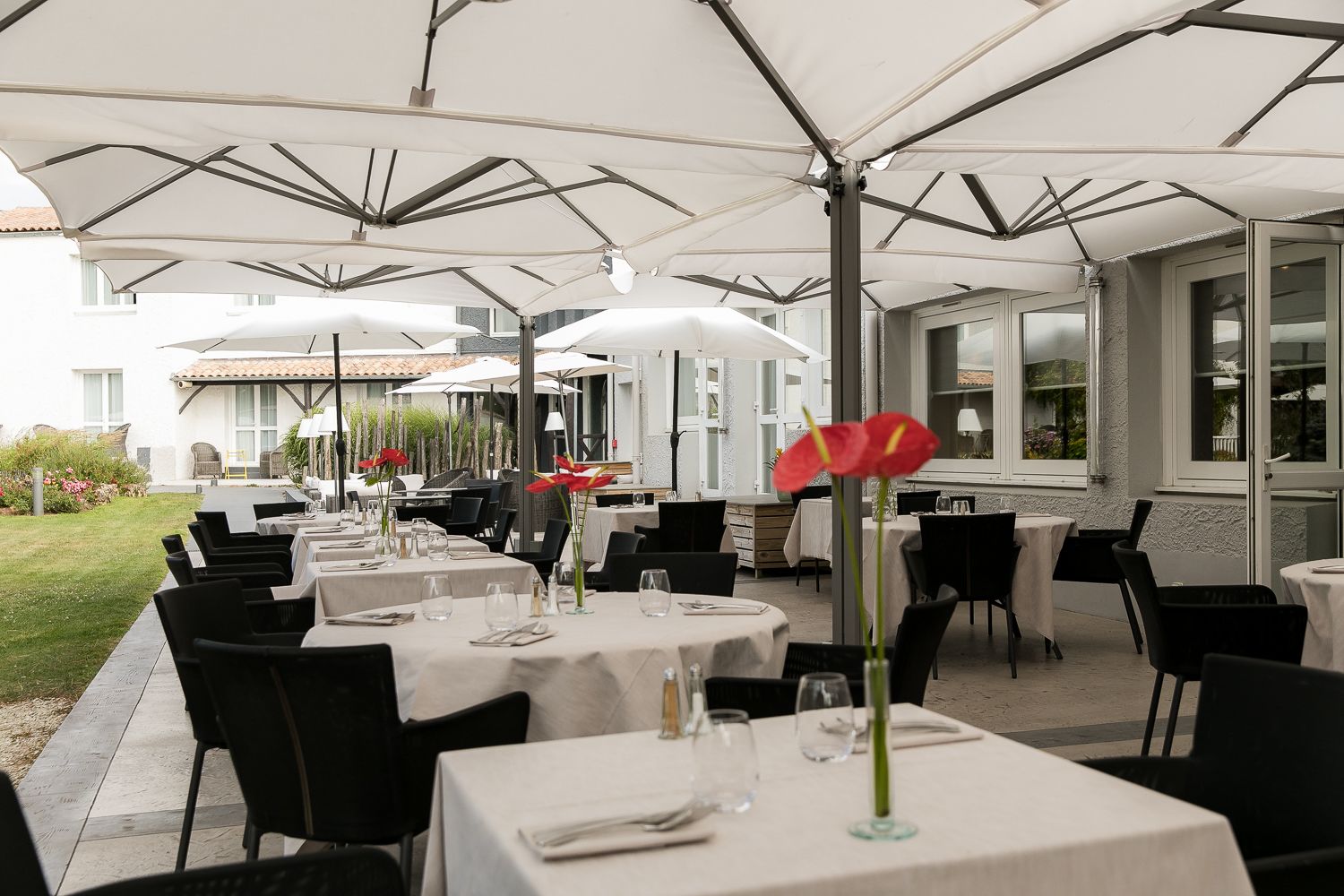 Een terras met tafels en stoelen onder witte parasols, omringd door een gebouw met grote ramen.