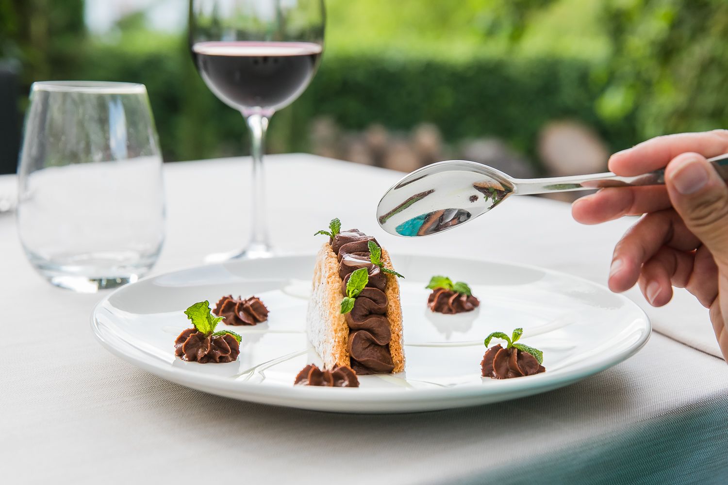A dessert plate with a chocolate mousse cake, mint leaves, and a spoon.