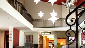 A spacious lobby with a high ceiling, a staircase with a decorative railing, and a restaurant in the background. - LOGIS HOTEL LE RABELAIS (Fontenay-le-Comte)