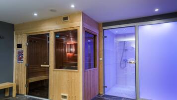 A sauna with wooden walls and a glass door, a shower area with blue-tinted glass, and a stone-tiled floor.