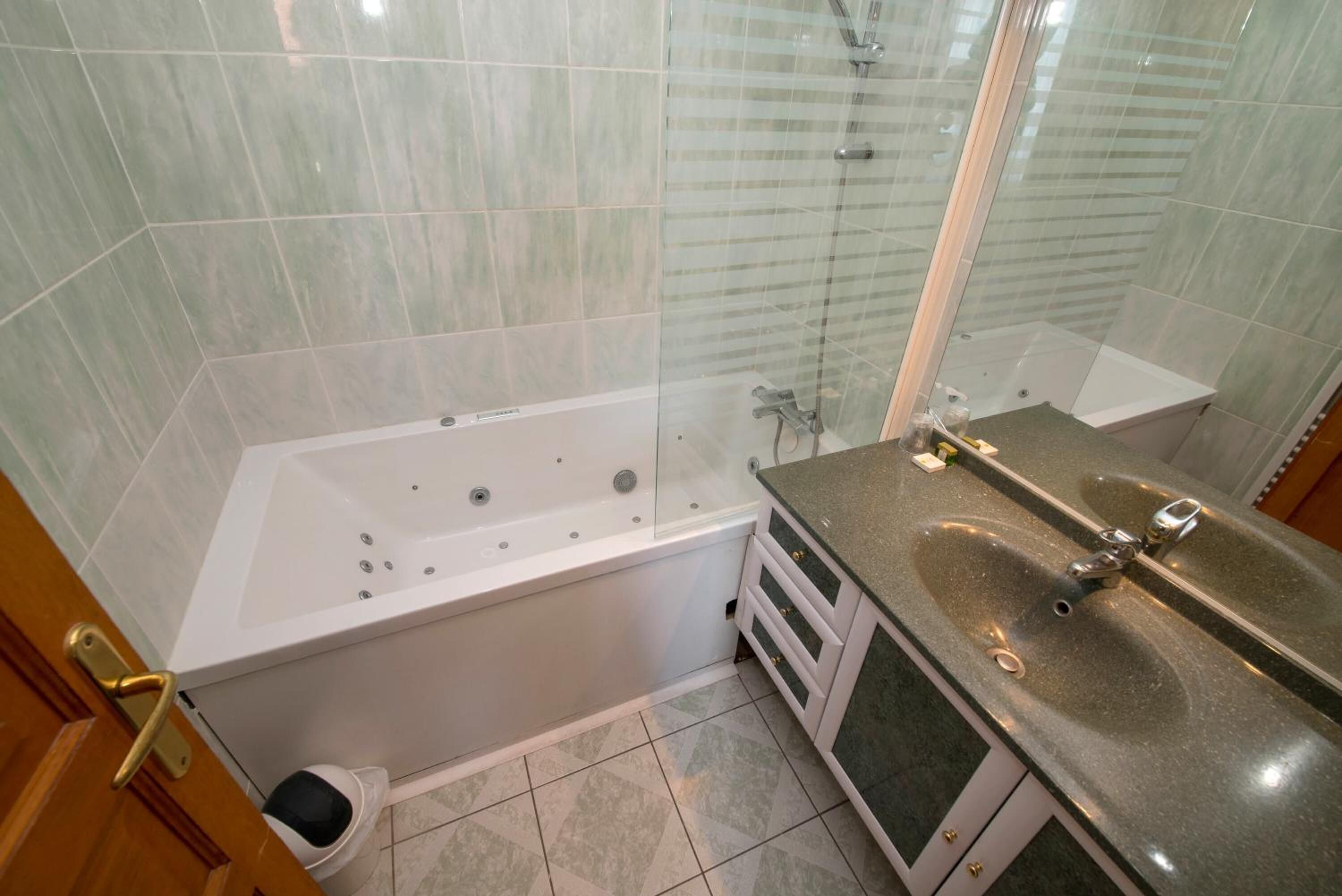 Un baño con ducha envuelta en vidrio, una bañera blanca y una encimera de granito con un lavabo.