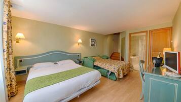 Une chambre d’hôtel avec un grand lit, un bureau avec un ordinateur et une chaise. On y trouve également une petite table sur laquelle sont posés une bouteille et un verre.