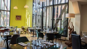 Un restaurante moderno con amplios ventanales, sillas verdes y una escultura de madera como pieza central.