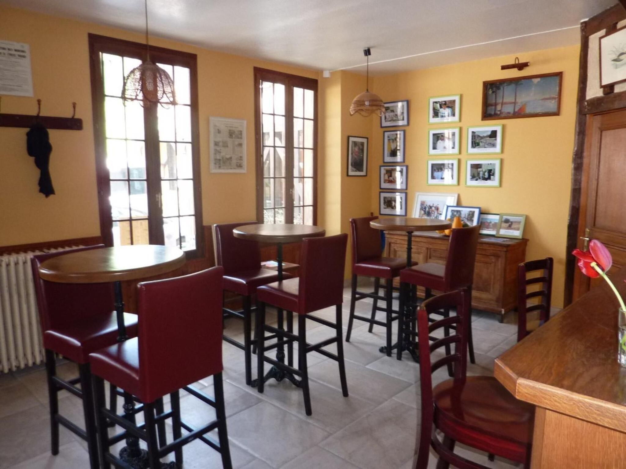 A dining area with red chairs and a wooden table, a window with a fan, and framed pictures on the wall.