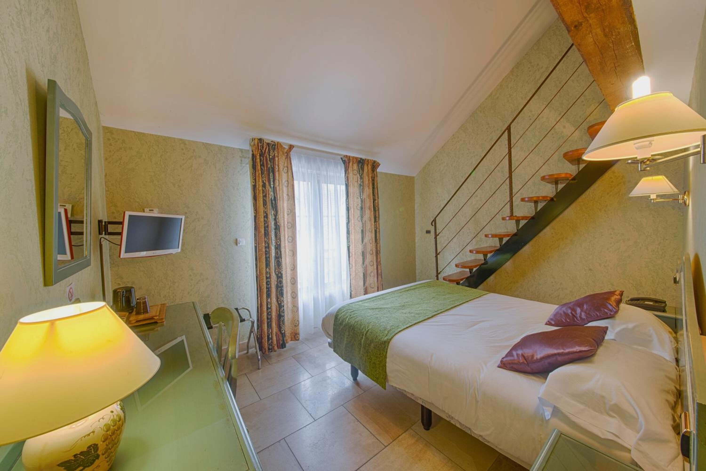 Een slaapkamer met een bed, een bureau met een lamp, een stoel, een televisie en een trap.
