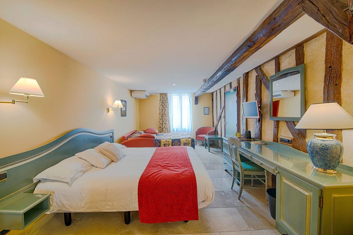 A hotel room with a bed, a desk, a chair, a mirror, and a window with curtains.