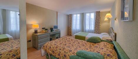 A hotel room with two single beds, a desk with a computer, a chair, and a lamp.