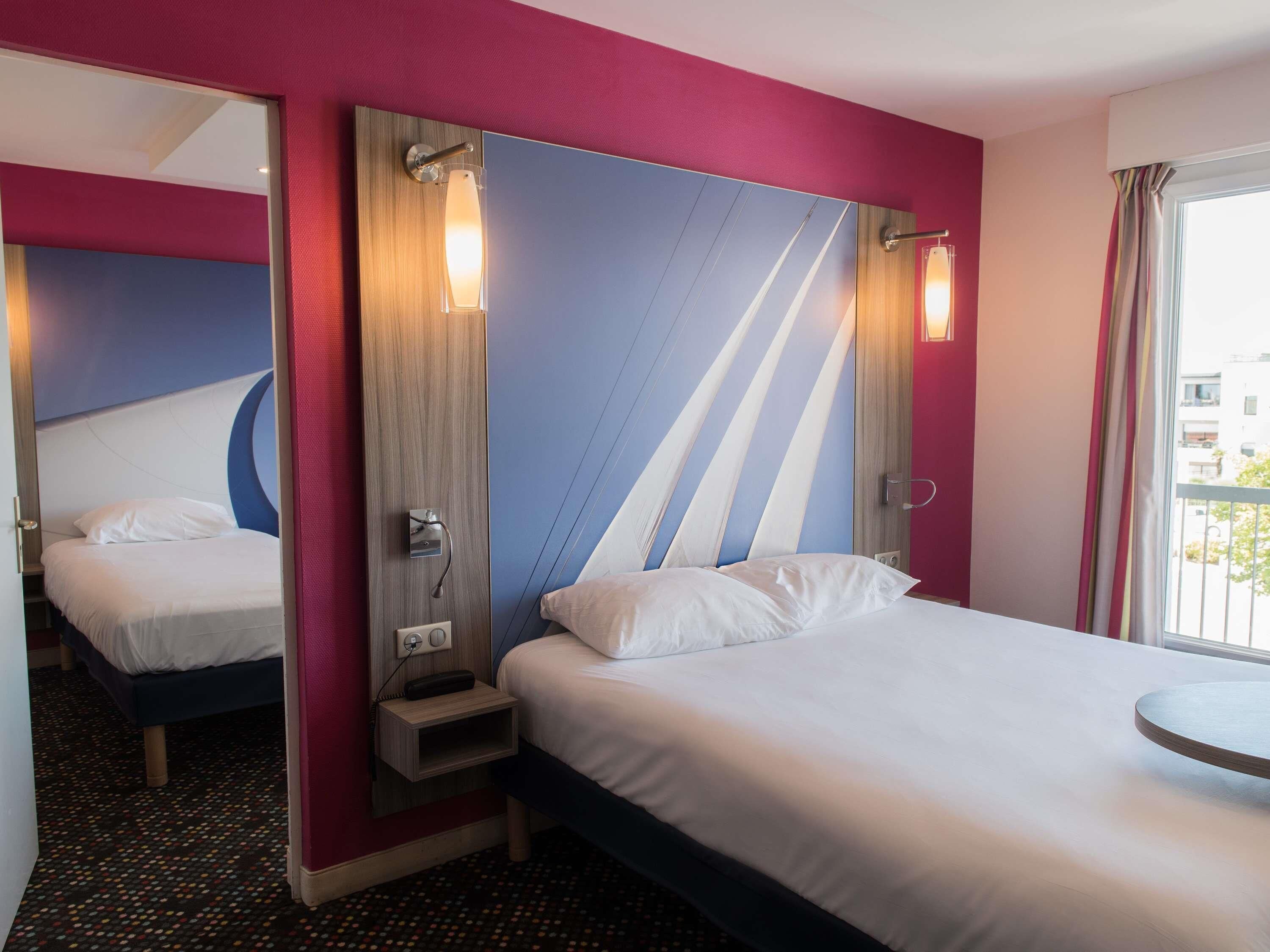 A hotel room with a bed, bedside table, and a mirror.