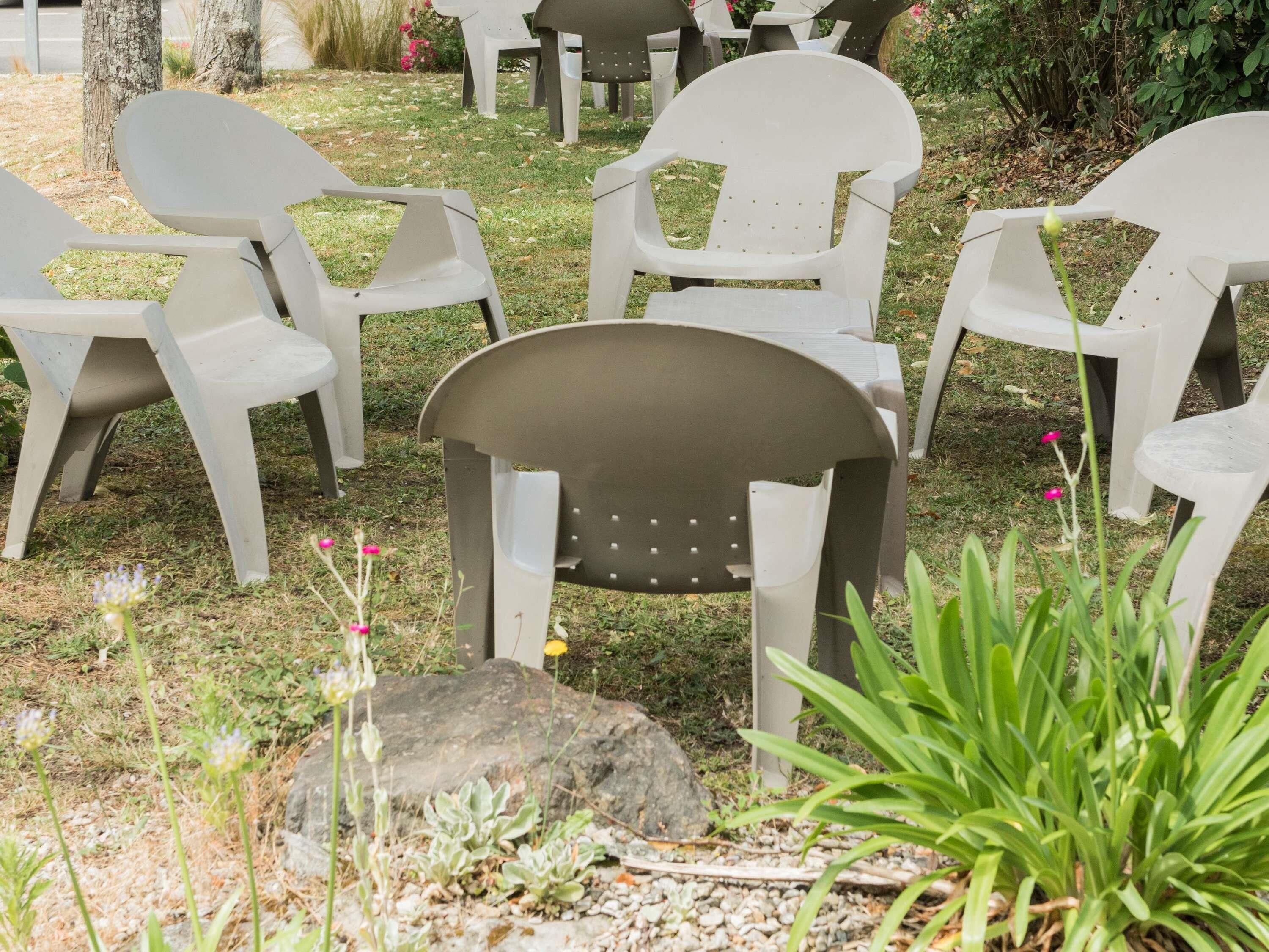 Espace extérieur aménagé avec des chaises en plastique disposées sur la pelouse, entouré de rochers et de plantes.