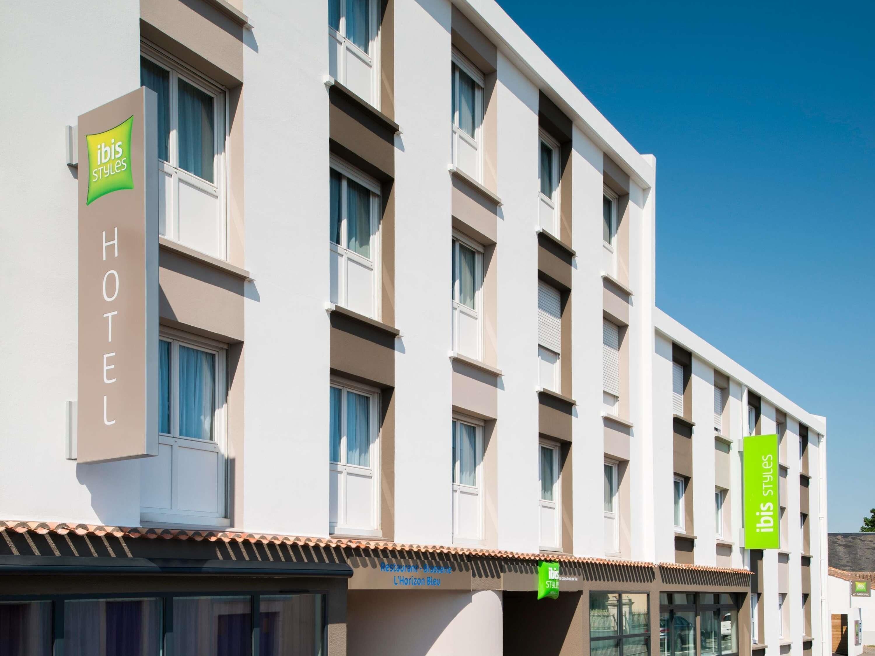 Un edificio de hotel con numerosas ventanas, un cartel con la inscripción 'ibis Styles' en la fachada, y un restaurante llamado 'L'Horizon Bleu' en la planta baja.