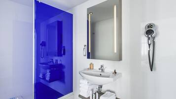 A modern bathroom with a glass shower enclosure, a white sink, a mirror, and a hairdryer.