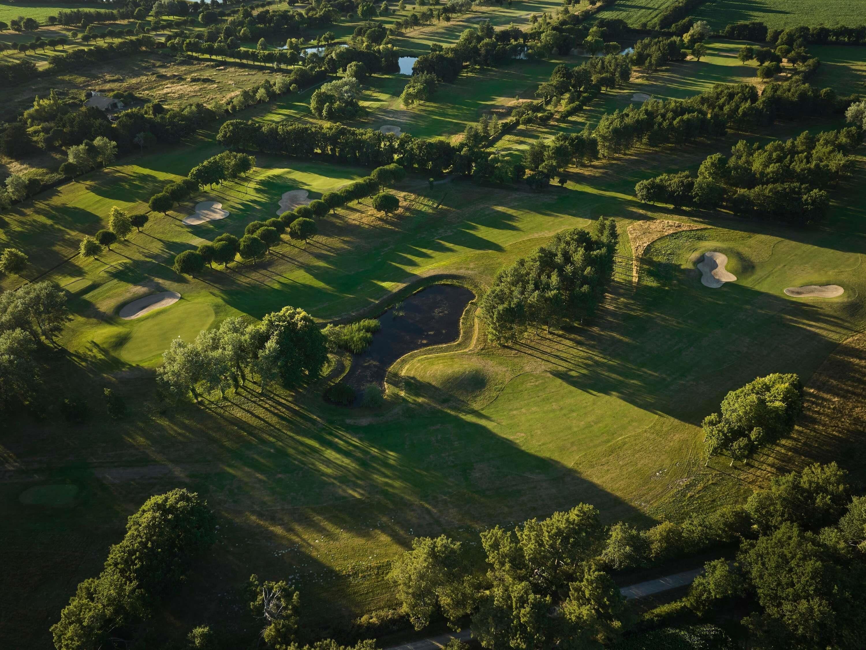 An aerial view of a golf course with multiple holes, trees, and a small pond.